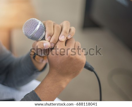 Hands holding microphone with blurred background and sun flare. Microphones are used in many applications such as telephones, hearing aids, public address systems for concert halls and public events.