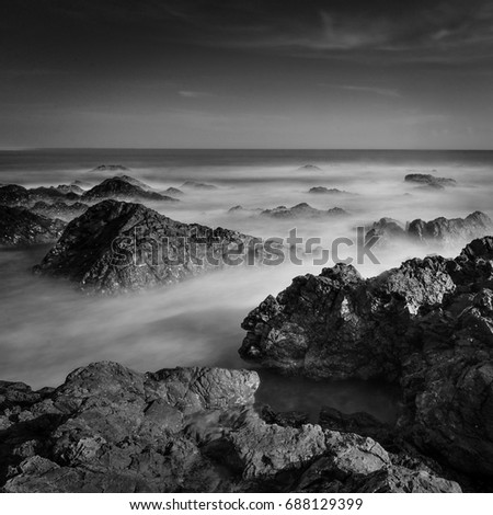 ropical rocky beach at sunrise in black and white, A slow shutter speed was used to see the movement of the clouds and the water 