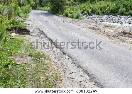 Narrow asphalt road near a creek with a paved on the shoulder