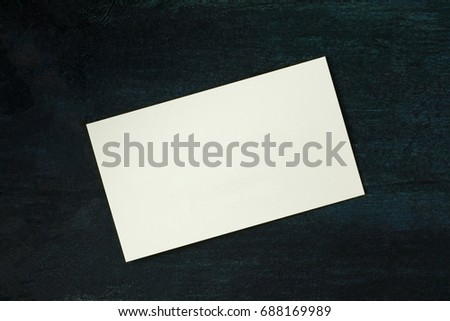 A photo of a blank white thick cardboard business card on a dark wooden background texture. A mockup or a minimalist banner with copy space
