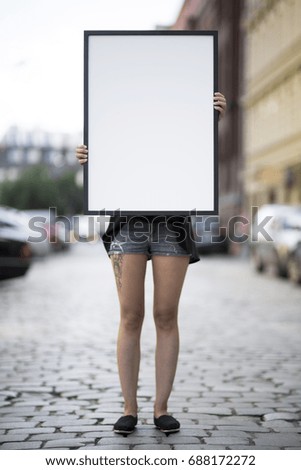 Girl holds a frame on the street for a poster presentation