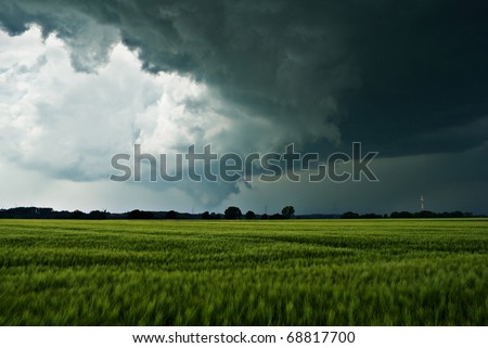 The image shows dark rainclouds over a field (barley) and was taken a few minutes after a small tornado. I'm not sure, but I think you can see the rest of the tornado. Royalty-Free Stock Photo #68817700