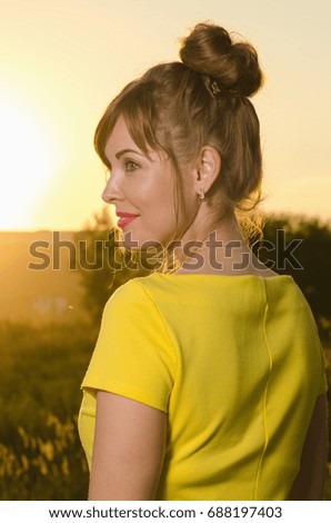 young woman walking on the field outside the city at sunset
