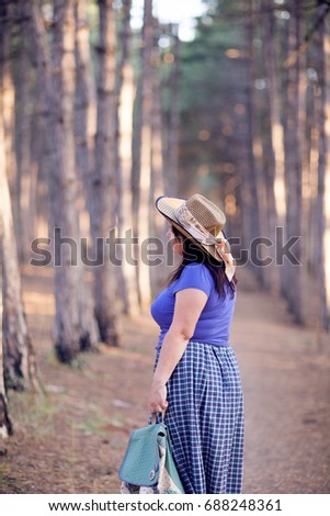 Happy senior woman in a straw hat with backpack walking through the forest. Nature outdoor activity. Healthy lifestyle concept.