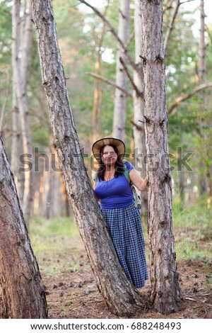 Happy senior woman in a straw hat with backpack walking through the forest. Nature outdoor activity. Healthy lifestyle concept.