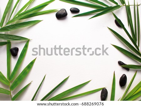 Bamboo leaf and sea pebbles background. White paper with tropical leaf ornament. Green bamboo leaf and sea beach pebbles flat lay. Blank page notepad top view. Natural spa or beauty banner template