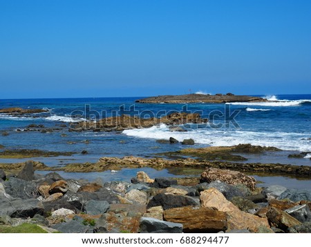 White wave foam of the blue ocean hitting the shore of a rocky beach in San Juan, Puerto Rico