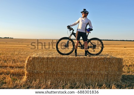 the cyclist with the bike resting on straw harvested field
