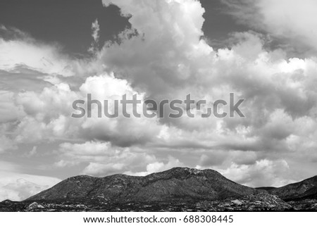 Black and white photo of huge puffy white monsoon clouds framing the Catalina Pusch Ridge mountains on a sunny day in Tucson Arizona