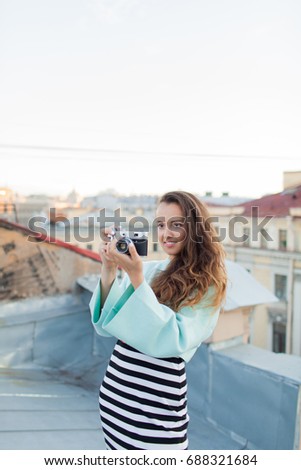 Fashion look, pretty cool young woman model with retro film camera. curly hair outdoors. Stylish girl photographer takes the old city from the roof at sunset.