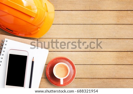 Safety helmet, blank paper notebook and smart phone on brown wooden table background in concept of education promotion advertising.Top view with copy space (selective focus). Office desk table concept