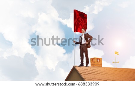 Businessman standing on house roof and holding red flag. Mixed media