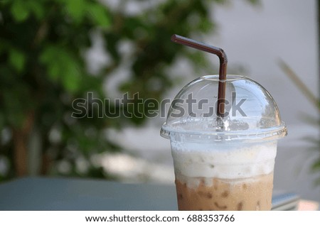 Close up ice coffee in the plastic cup with brown straw and out focus notebook, start work in a refresh morning.