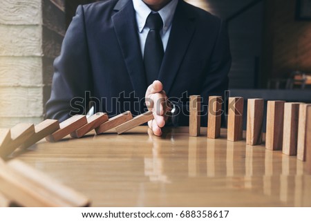 Close up of businessman hand Stopping Falling wooden Dominoes effect from continuous toppled or risk, strategy and successful intervention concept for business. Royalty-Free Stock Photo #688358617
