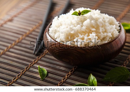 Cooked white rice (Thai Jasmine rice), rice in dark wooden bowl with chopsticks on the wood black bamboo background. Royalty-Free Stock Photo #688370464
