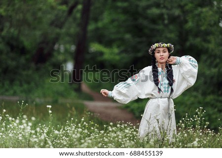 Beautiful brunette girl  with two pigtails hair braids wearing national Ukrainian costume and flower wreath, walking in the forest