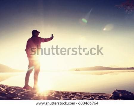 Side View of Man Taking Selfie Photos at the Beach. Hot morning Sun rising over mountain lake.