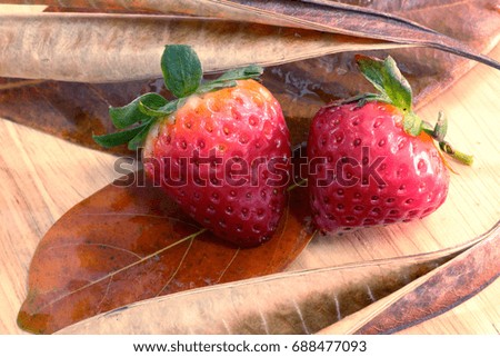 focus at two strawberries and dried leaves on wood background