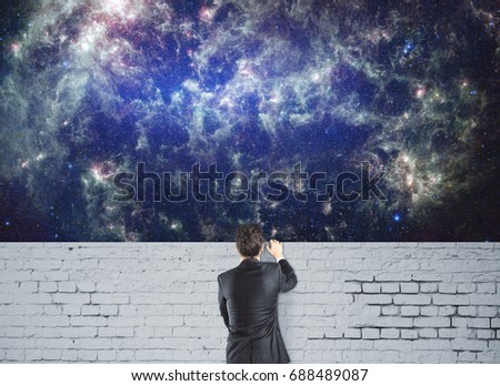 Back view of young businessman standing behind white brick wall and looking at space cosmos sky. Universe concept. Elements of this image furnished by NASA