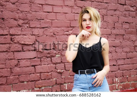 a young girl stands on the street against the red brick wall
