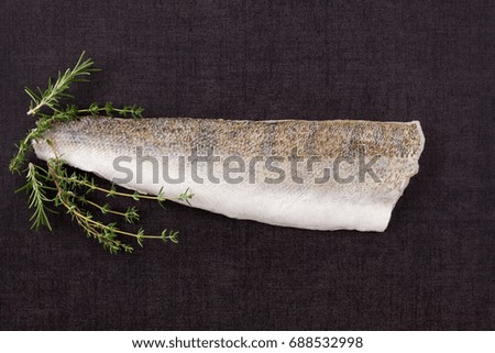 Fresh Fillet fish slice with thyme and rosemary on black surface from above. Culinary seafood eating. 