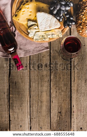top view of bottle of red wine, wineglass, different cheese and bread on wooden tabletop with copy space
