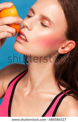 Young fashion woman with juicy orange on a blue background with copyspace and bright clothes. Bright makeup and juicy colors