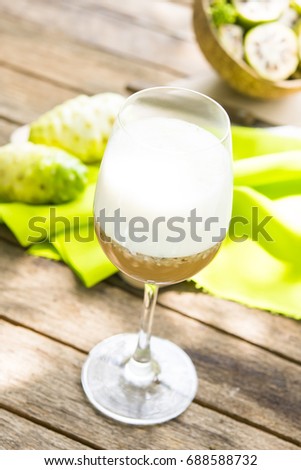 Noni juice with noni fruit and noni slices in coconut shell on wooden background.