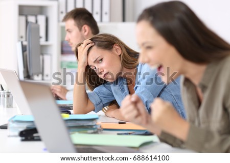 Worried worker beside a successful one who is excited reading good news on line at office Royalty-Free Stock Photo #688614100