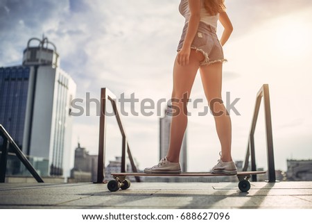 Young woman is posing with skateboard in the city. Female outdoor with long board.