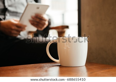 front view. young business man holding tablet for checking stock graph. have coffee cup with coffee putting on table front of him. image for beverage,technology,mobile,body part concept
