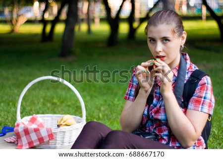 Young woman in plaid shirt playing on the ocarina in the park. The girl is sitting on the green grass, picnic.