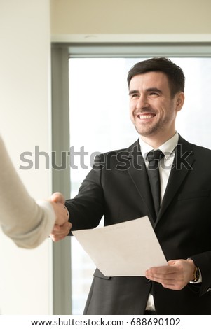 Happy smiling businessman wearing suit shaking female hand, holding document, company director congratulating new hire employee offering employment contract, awarding with diploma, vertical view