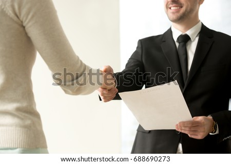 Employment handshake, smiling friendly employer shaking new hire hand, happy businessman holding document, giving official paper to businesswoman, offering job contract, focus on hands, close up view Royalty-Free Stock Photo #688690273