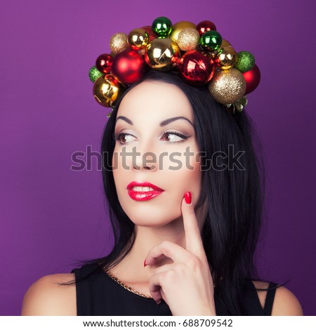 beautiful woman wearing a wreath made from Christmas decorations and looking at Christmas decorations hanging on Christmas tree