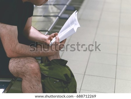 Seated man in shorts and t-shirt with a bag, reading a book. Selective focus. Lifestyle concept.