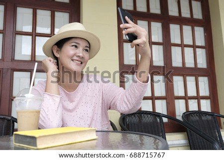 Portrait of beautiful middle age asian women is drinking ice coffee and taking photo myself be smartphone at cafe 
