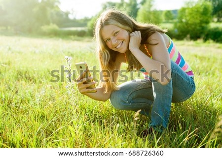 Young teenage girl using a smartphone, photographing a flower in a park. For your page in the instagram