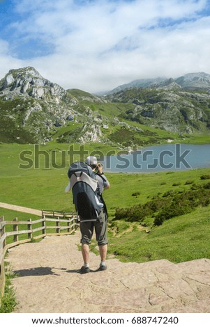 Family trip to Spain nature: father with a baby in a backpack hiking on the trail to high mountain lakes in sunny summer day