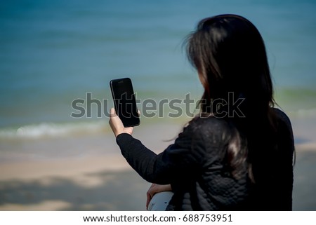 Black hair girl is holding a phone up to take a picture of the sea,Beach vacation.
