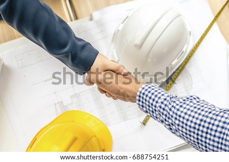 Close-up of business people handshaking at background over helmets, documents, worker tool