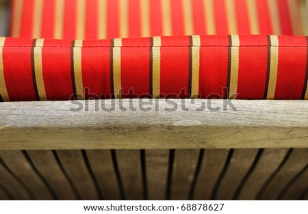 Abstract detail photo of the back of a wooden bench with cushion of red and yellow stripes