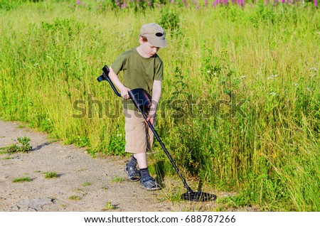 serious boy with a metal detector examines the soil on a rocky trail on a summer evening