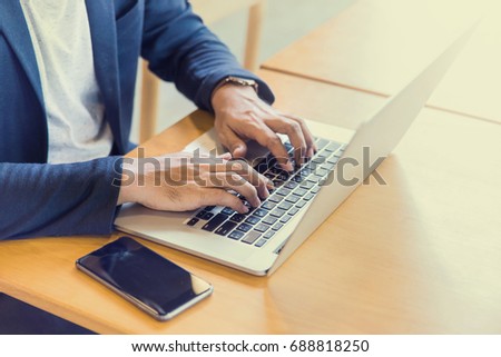 young man, wearing glasses and smiling, as he works on his laptop to get all his business done early in the morning