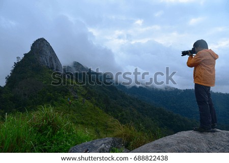 The traveler with DSLR camera take picture  with mountain background in rainy season