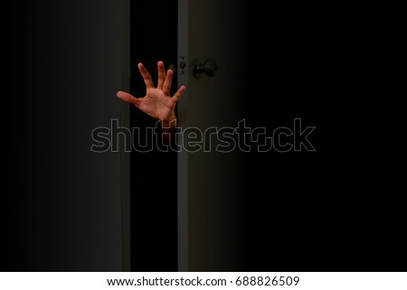 The hand protrudes from the outside of the door in the dark. Concept of Halloween.