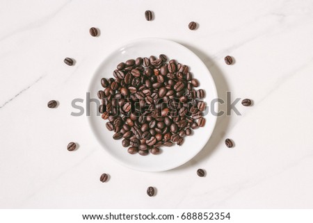 Coffee beans shoot close-ups in a white bowl on a white slate floor close to.