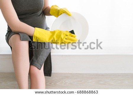 Pregnant woman tiredly washes a plate, close up picture. Housework routine, cleaning and household concept during mother-to-be period
