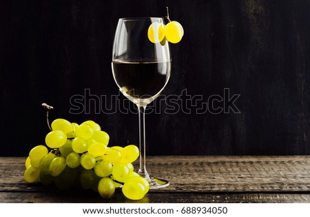 Glass of wine and a vine on the background of a dark rustic tree. White grape wine and grapes.