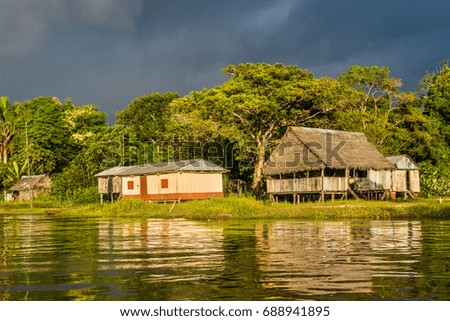 Village with huts and wooden buildings on Amazon with late afternoon sunshine and dark stormy sky
